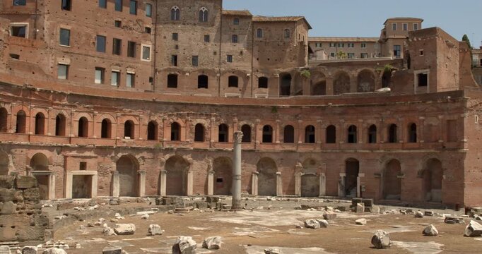 View of Trajan's Market in Rome, Italy, showcasing the semi-circular brick exedra with layered ancient arches, historic windows, and scattered archaeological remains in a sunny summer morning.