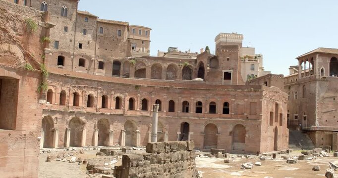 View of Trajan's Market in Rome, Italy, showcasing the semi-circular brick exedra with layered ancient arches, historic windows, and scattered archaeological remains in a sunny summer morning.