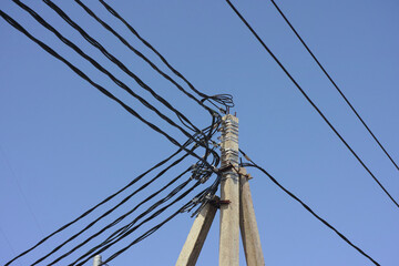 Fototapeta premium Low-angle shot of a concrete utility pole with a complex tangle of black electrical power lines against a clear blue sky background.