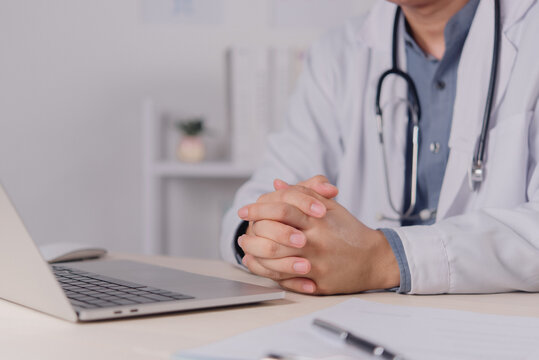 doctor physician wearing white coat stethoscope sitting hands clasped desk clinic office hospital healthcare worker professional medical consultation patient empathy attention support health care