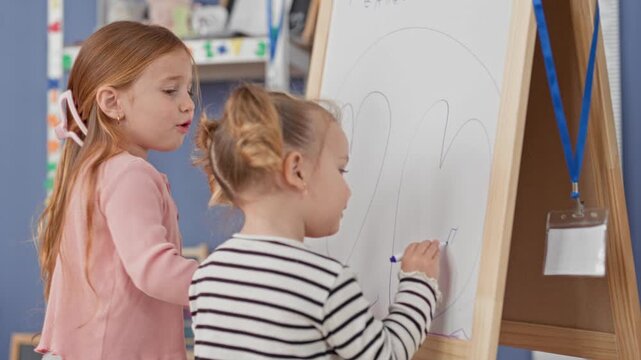 Little girl drawing on whiteboard easel, marker in hand inside a classroom building; early learning curiosity.