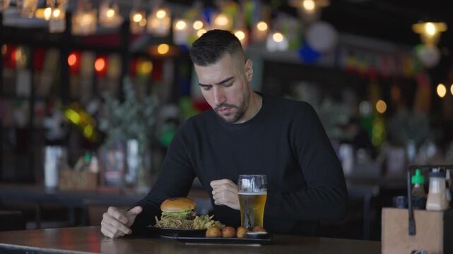Smiling Man Eating a Gourmet Burger with a Beer in a Cozy Restaurant
