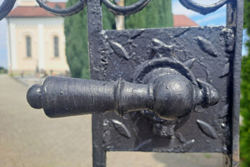 Fototapeta premium Close-up of antique wrought iron gate handle with blurred church in background.