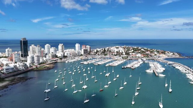 High aerial panoramic view of Punta del Este marina filled with luxury yachts and sailboats, featuring the city&rsquo;s skyline, blue Atlantic Ocean and clear summer sky in Uruguay.