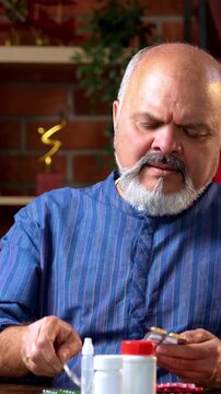 Indian senior retired man takes prescribed medicine or pill daily as part of his health routine while sitting at home desk