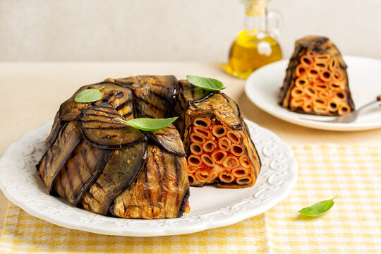 Eggplant Timbale or Timballo di Melanzane. Grilled eggplants wrap around the pasta and tomato, cheese sauce, and baked. Italian meal. Table with yellow tablecloth.