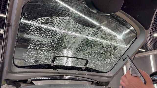 Professional car window tinting process: technician prepares the glass, applies tint film, uses a heat gun to shape it on curved surfaces, and smooths out air bubbles with a squeegee. 