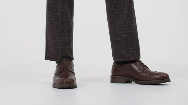 Businessman's legs tapping nervously in brown brogue shoes and checkered trousers on white background