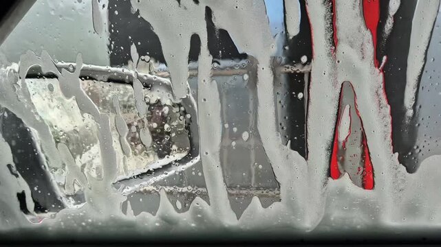 View from inside a car window looking at running water and white soap foam during a car wash