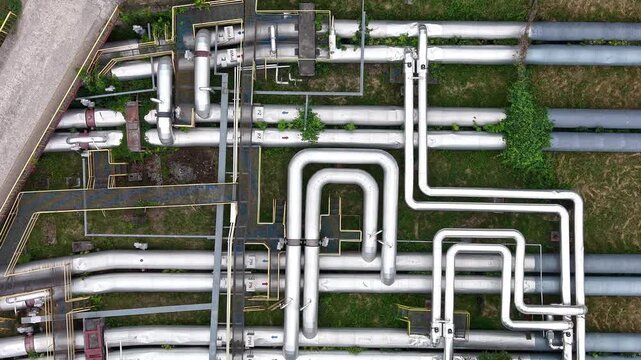 Aerial view of interconnected industrial pipelines with green vegetation and yellow markings, showcasing the complex layout of the piping system across a grassy area