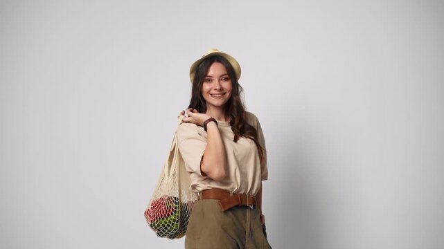 Woman holding reusable string bag with fresh groceries isolated on white background. Zero waste and conscious consumerism