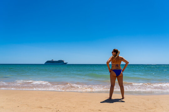 Beautiful middle-aged woman standing on seashore looking at cruise ship in summer.  Back view. Cruise vacation