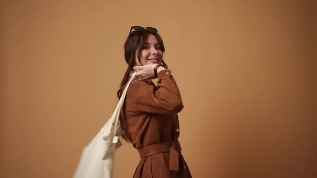Stylish smiling woman walking with an eco-friendly tote bag for conscious shopping and sustainability on a brown background