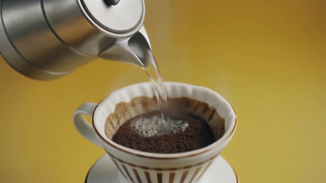 Stainless steel kettle pouring hot water into a ceramic coffee dripper for a morning caffeine ritual video motion clip