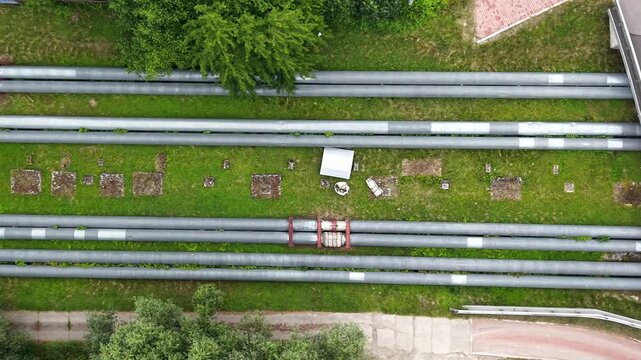 Aerial view of industrial pipes arranged in parallel lines across grassy terrain, showcasing the continuous flow and connection of gas and water infrastructure in an outdoor setting