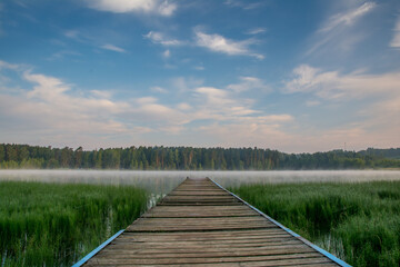 Obraz premium Misty Sunrise Over Wooden Pier on Calm Forest Lake, Central Russia