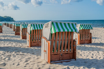 Traditional German hooded beach chairs Strandkorb lined up on a sandy sea coast under a blue sky. © Анастасия Константне