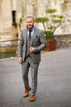 A man with a beard in a strict grey three-piece suit with a tie in the old town of Sirmione, a Stylish man in a grey suit in Italy