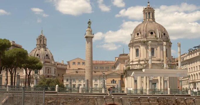 Beautiful panorama of Trajan's Column standing between the twin churches of Santa Maria di Loreto and Santissimo Nome di Maria at the Trajan's Forum under a cloudy blue sky in Rome, Italy.