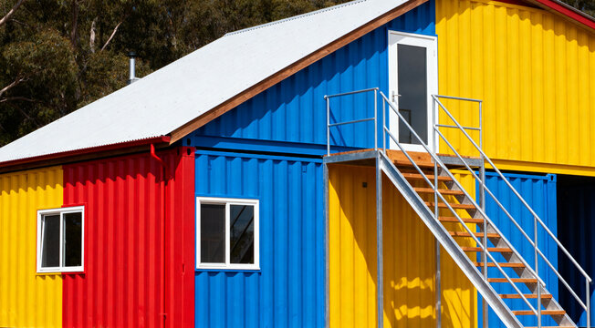 Modern prefab container house painted in bold colors with outdoor stairs and balcony access.