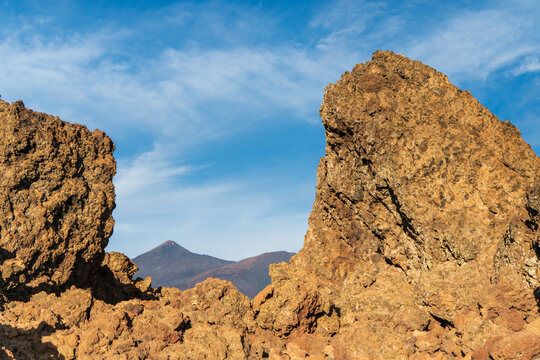 Dramatic volcanic rock formations frame Mount Teide under a clear blue sky