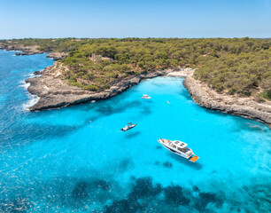 Aerial view of Cala Mondrago bay in Mallorca, Spain. Luxury yachts, boat anchored in turquoise sea water cove, rocky coast with green pine trees, sand beach on sunny day. Mediterranean drone landscape © den-belitsky