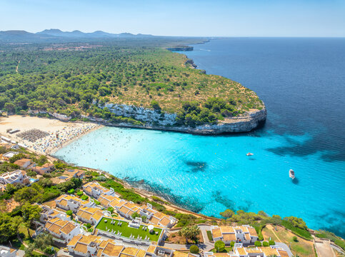 Aerial view of sandy beach and sea bay in Mallorca, Balearic islands, Spain. Top view of turquoise water, boats and yachts, resort hotels, green trees on rocky cliffs. Mediterranean landscape. Summer