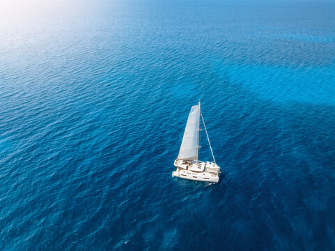 Aerial drone view of luxury sailing catamaran yacht moving in blue sea. Summer vacation and travel. Top view of modern sailboat cruising in Mediterranean sea. Yachting in Mallorca island, Spain.