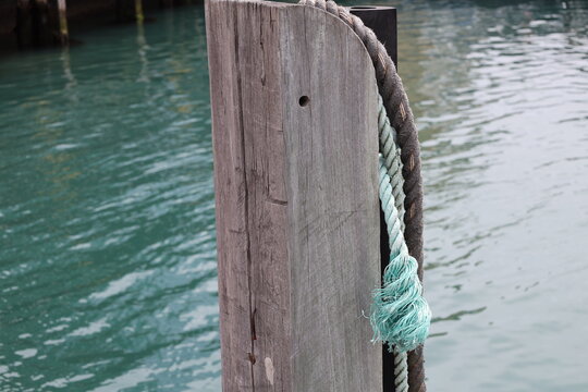weathered wooden marina bollard, thick, grey-brown rope coiled, lighter blue-green faded section at frayed end (close-up, harbor, maritime, dock) 4677