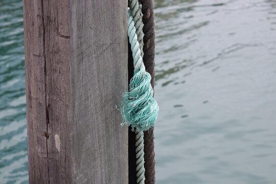 weathered wooden marina bollard, thick, grey-brown rope coiled, lighter blue-green faded section at frayed end (macro, close-up, harbor, maritime, dock) 4678