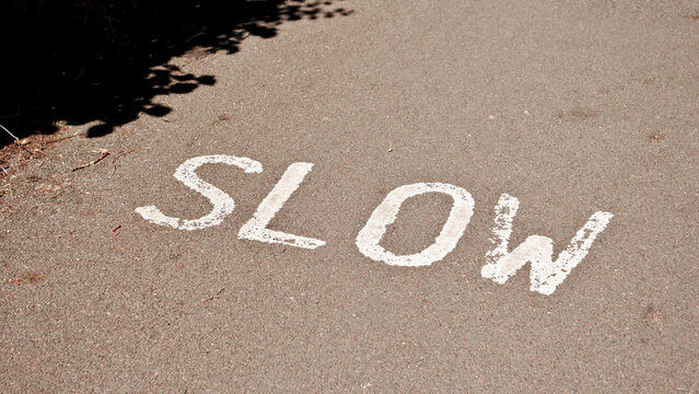 Slow road marking painted in white on asphalt surface, traffic safety sign on pavement, cautionary speed regulation text on pathway close up