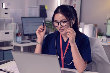 Smiling doctor attending an online consultation with a laptop in a modern clinic, promoting...