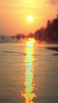 Close-up of gentle sea waves washing onto a sandy beach during golden hour sunset. Beautiful low-angle view with shallow depth of field, Peaceful mood of a summer vacation at the tropical shore.