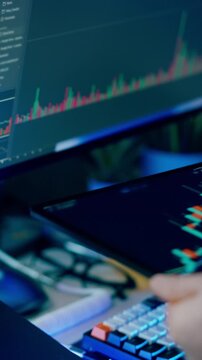 analyst hand holding a tablet and pointing with digital pen  dynamic candlestick chart displaying stock market price trends. In the background another screen blurred multi colored financial graphs