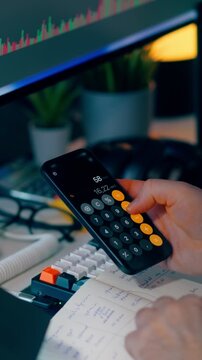calculator analyzing financial notes bills. Close up businessman finger presses buttons on smartphone calculator application screen. The table workspace contains  colorful keyboard open budget ledger