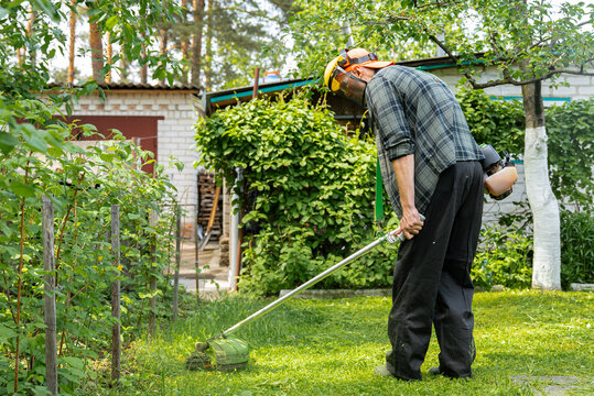 Man using grass trimmer in lush garden setting