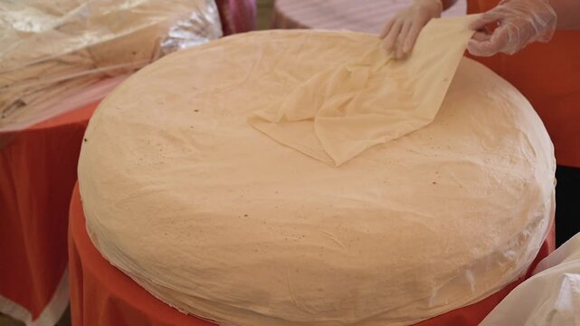 Bakery worker wearing protective gloves carefully handles and folds a thin layer of traditional Turkish yufka dough at local market. Slow motion video footage