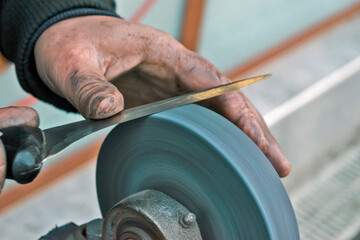 Fototapeta premium Experienced craftsman sharpening a steel knife by hand