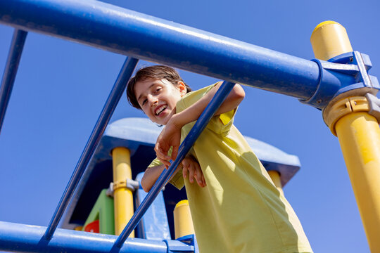 Smiling boy on playground climbing frame under blue sky