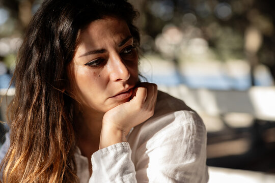 Thoughtful woman resting chin on hand in warm sunlight