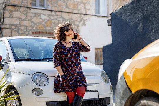 Woman talking on phone by compact car in sunny street