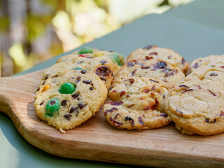 Fototapeta premium Main servant un assortiment de cookies artisanaux sur une planche en bois lors d’un buffet de desserts ou d’un événement en extérieur