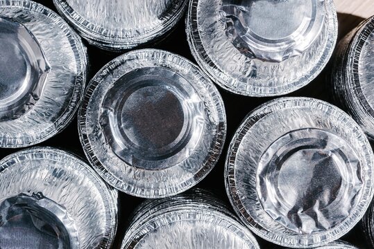 Stack of empty aluminum food containers. Circular metal foil trays for waste sorting and recycling. Industrial material management, zero waste lifestyle and sustainability concept.