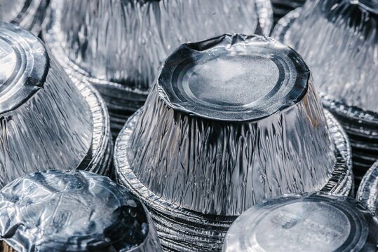 Stack of empty aluminum foil containers for food. Metallic circular trays for recycling and waste sorting. Industrial material collection, environmental sustainability and metal repurpose.