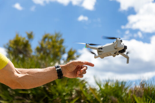 Person reaching toward flying drone in sunny park sky