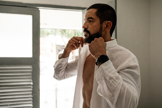 Authentic lifestyle moment of a man dressing at home before leaving, emphasizing personal style and preparation.
