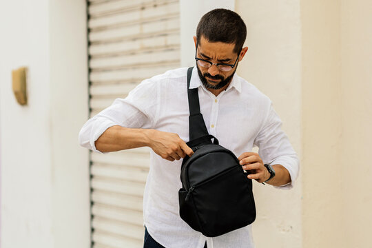 Stylish mature man with crossbody bag walking through urban neighborhood showing authentic everyday fashion and relaxed lifestyle.