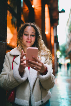 Smiling traveler browsing on smartphone in evening urban setting, mobile navigation application, wireless communication, youth using cellular network, digital lifestyle, modern tech device.