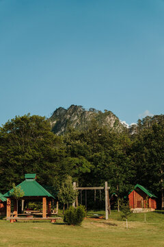 Wooden camping cabins and picnic shelter surrounded by lush forest and open meadow. Peaceful destination for outdoor recreation, hiking, and nature holidays.
