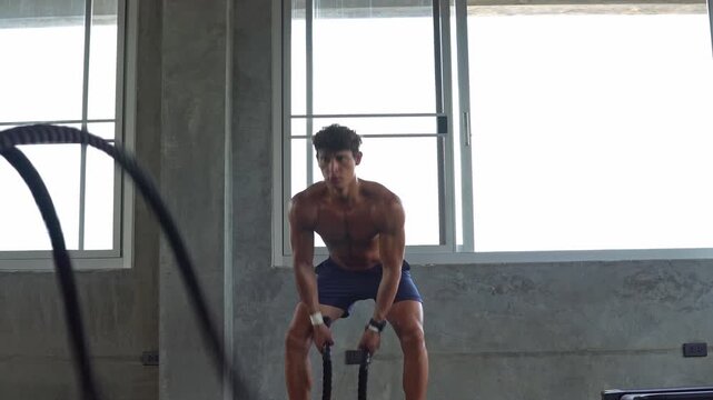 Strong muscular man training with battle rope in gym fitness. exercise concept to push the limits of power strength. topless men workout for better health and quality of life.